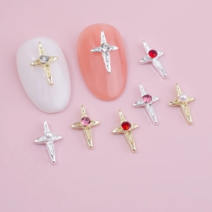 Close-up of cross nail charms with rhinestones and pearls on a soft pink background