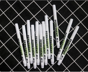 Flat lay view of white permanent markers with 1.0mm tip on a checkered fabric background