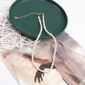 Macro detail of natural baroque pearl necklace with gold clasp on green tray