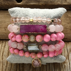 Detail of pink bohemian stacked bracelets with crystal charms on a velvet pillow