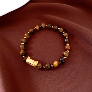 Détail macro de perles œil de tigre avec breloque tigre plaquée or sur soie rouge