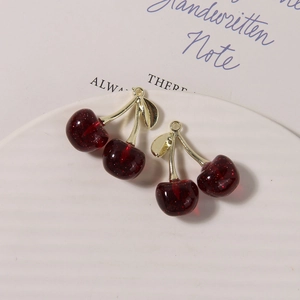 Detail of red glitter resin cherry charms with golden metal leaves on a white plate
