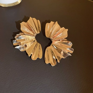 Macro detail of gold-plated earrings with abstract pleated petal texture on leather