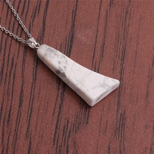 Gros plan d'un pendentif en marbre blanc trapézoïdal avec chaîne en argent sur bois