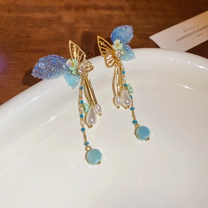 Detail of gold butterfly tassel earrings with blue sequins and drop pearls on ceramic tray