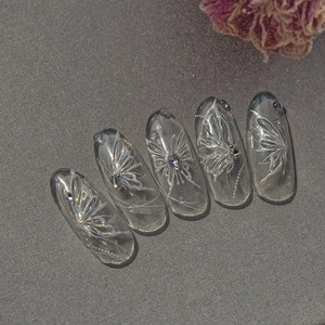 Detailed view of translucent press-on nails with white butterfly patterns and rhinestones