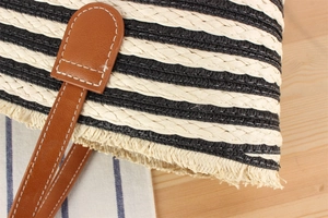 Close-up of black and white striped straw bag with brown leather handles and white stitching