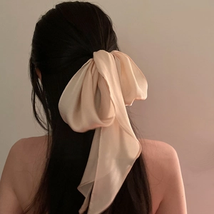 Detail of a large beige silk bow hair clip with soft satin texture on a model