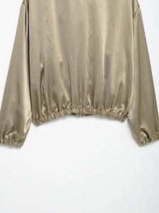 Detail view of the elastic hem and zipper on this cropped brown satin jacket top
