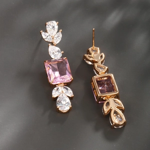 Macro shot of gold-plated geometric earrings with pink square stones and white pear accents