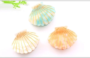 Detail view of shell-shaped hair claws in mint, pearl white, and peach with gold accents