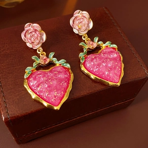 Close-up of vintage heart earrings with pink resin flowers on a leather jewelry box
