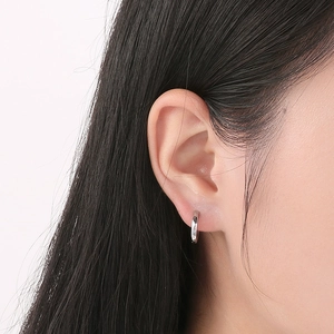 Close-up of minimalist silver stainless steel hoop earrings worn on a model's ear