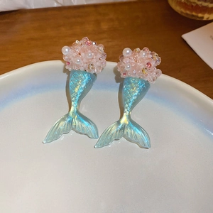 Detailed close-up of pearl flower and gradient blue mermaid tail earring on ceramic