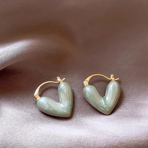 Macro shot of gold hoop earrings with green marble inlay on champagne silk background