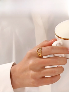 Golden hollow heart ring worn by model holding coffee cup in a lifestyle setting