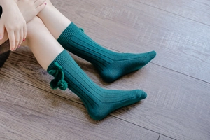 Close-up of deep green knitted knee-high baby socks with pompom and bow details