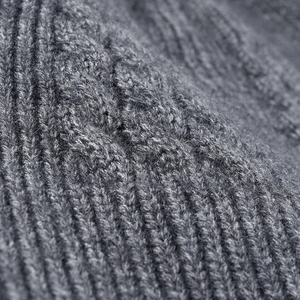 Close-up van de dikke grijze kabelgebreide textuur van een warme wintermuts