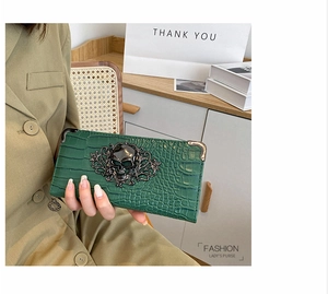 Macro view of dark green crocodile texture purse with metal skull and corner protectors