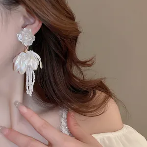Elegant white floral tassel earrings with silver pins and beads on female model
