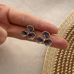 Detail of hand-held purple floral stud earrings with sparkling crystal center