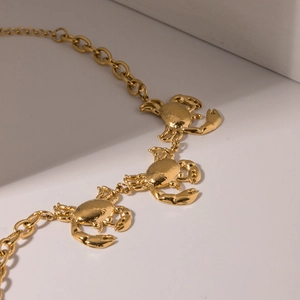 Macro detail of three golden crab charms on a polished titanium steel bracelet