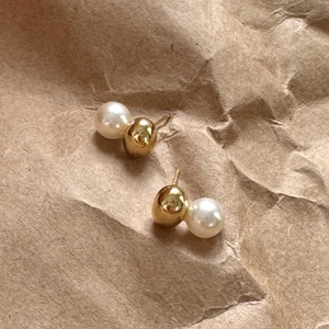 Detail of asymmetric pearl and gold ball stud earrings on textured brown paper