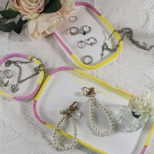 Detailed arrangement of silver rings and pearl charms on white oval resin jewelry trays