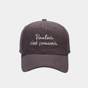 Macro detail of white embroidery on dark gray cotton baseball cap featuring French text