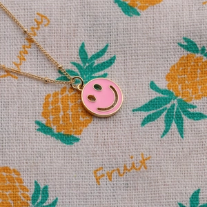 Close-up of pink enamel smiley face pendant with gold plated chain on fruit pattern background