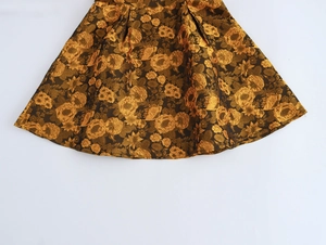 Detail van een elegante goudkleurige jacquard mini-jurk met bloemenpatronen en plooien