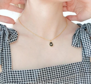 Detail of a gold stainless steel necklace with a black butterfly oval pendant on a model