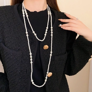 Collana a doppio filo di perle irregolari con pendente a moneta d'oro su giacca nera