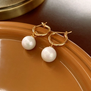 Close-up of golden hoop earrings with large white pearl pendants on a luxury tray