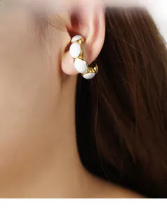 Detail of 18K gold-plated ear cuff with white enamel beads on a female model's ear