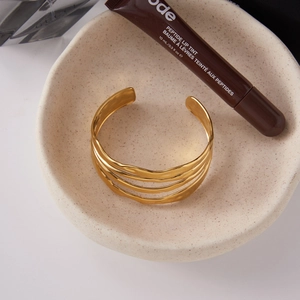 Detail of a luxury gold layered wave bangle on a ceramic tray with designer accessories