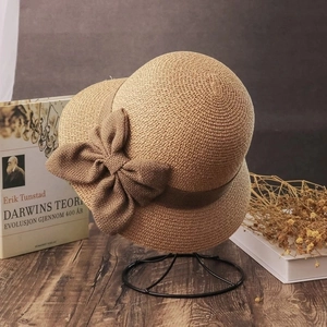 Detail of khaki straw sun hat with woven texture and a large decorative bow on side