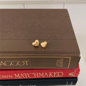 Detailed macro of golden heart earrings with 3D bow texture on stack of books