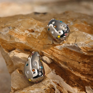 Macro shot of silver teardrop earrings with multi-colored crystals on a natural stone base