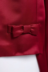 Detailed view of elegant red satin blazer featuring a decorative bow tie waist detail