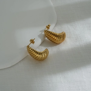 Close-up of golden chunky croissant hoop earrings with a textured ribbed metal finish