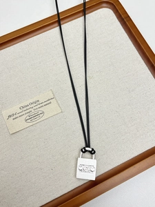 Macro detail of a silver padlock pendant with floral heart engraving on a black woven cord