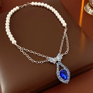 Detail of vintage necklace with pearl chain, blue bow and teardrop gemstone on leather box