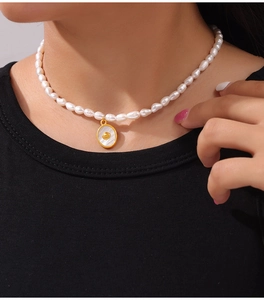Detail of freshwater pearl necklace with gold oval shell pendant on model neck