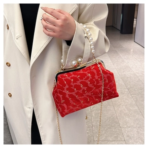Detail of red velvet shell bag featuring pearl handle and golden vintage patterns