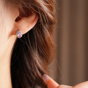 Close-up of elegant silver stud earrings with purple oval cubic zirconia on model ear