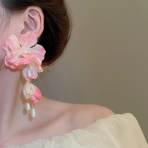 Close-up of pink fabric flower earrings with pearl tassels on a model for a chic look