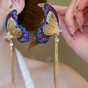 Detail of purple embroidered butterfly earrings with gold tassels and crystals on model