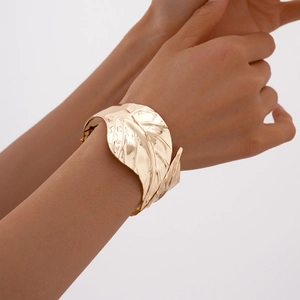 Detailed view of golden leaf texture on wide open cuff bracelet with metallic finish