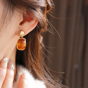 Close-up of 18K gold plated amber resin drop earrings worn by a model in soft light
